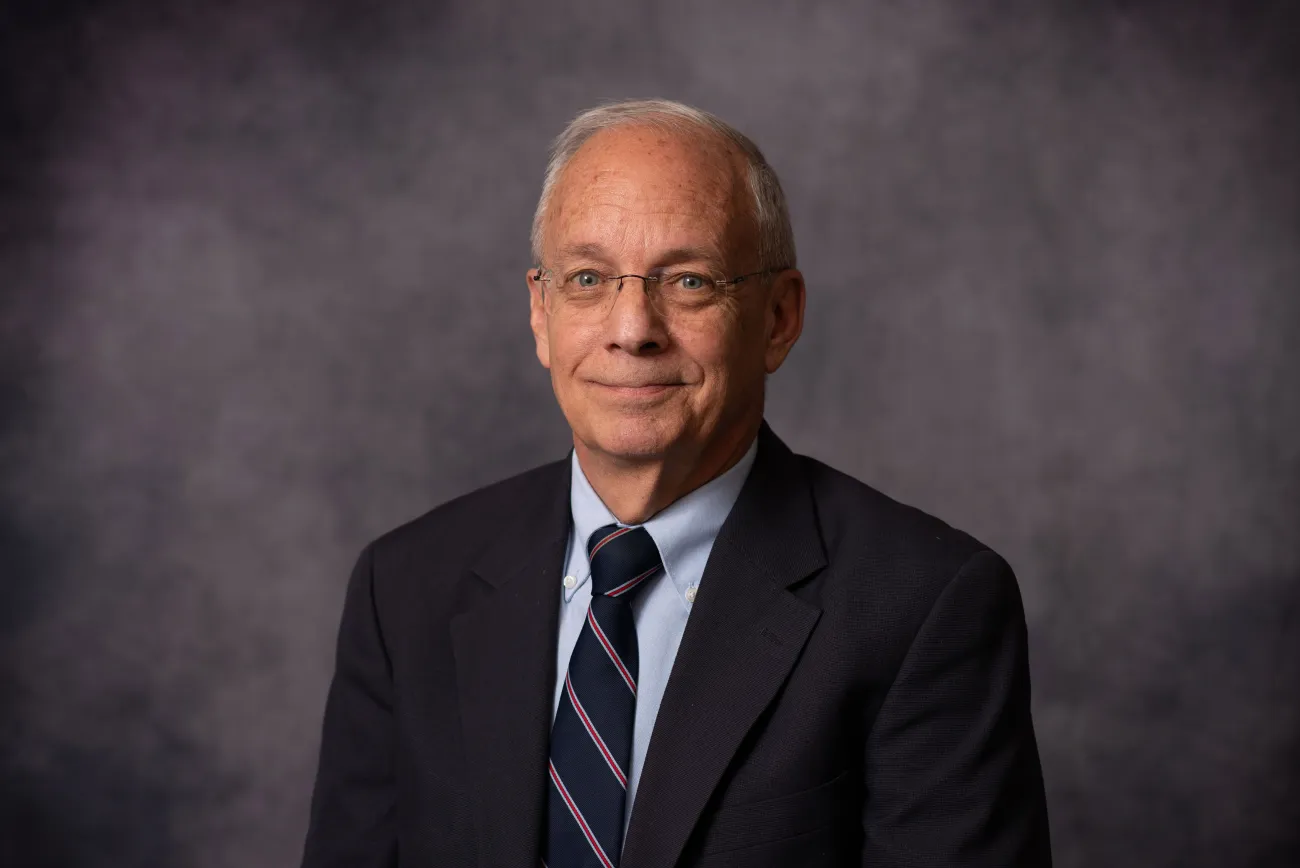 A portrait of interview subject Steve Parker, who wears a dark suit and tie and is seated in front of a gray background